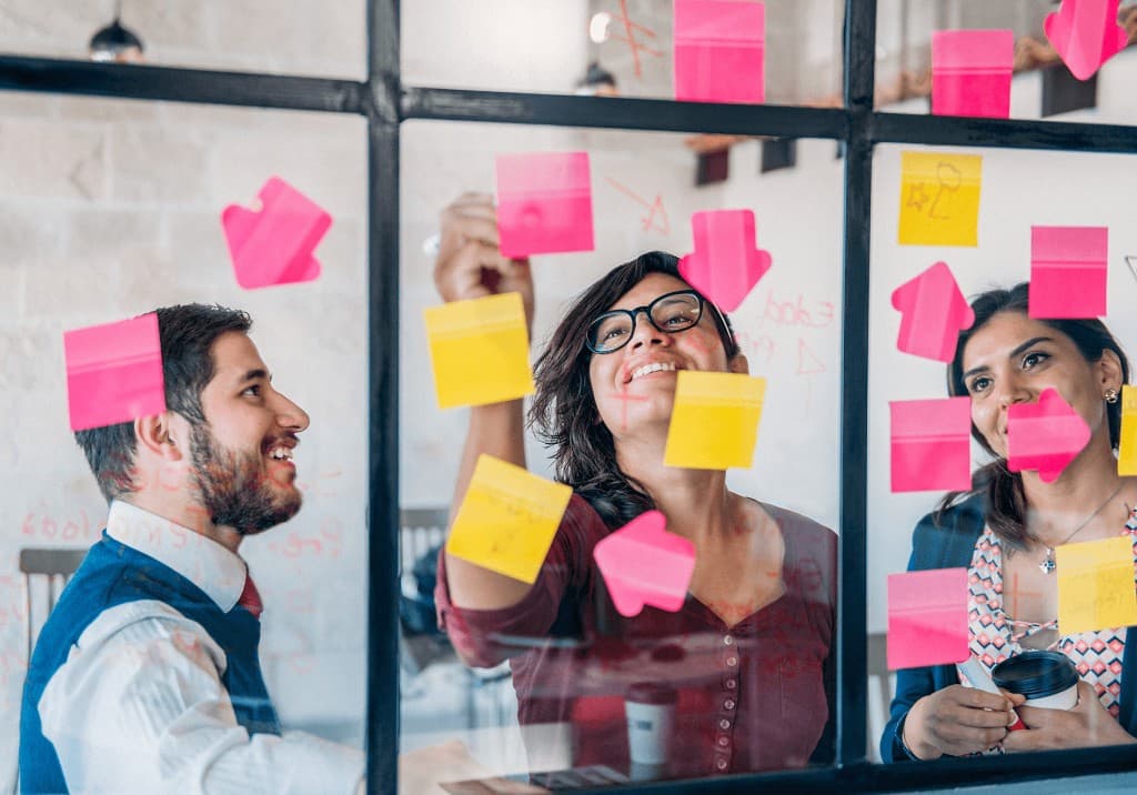 Team placing sticky notes on a glass wall while planning