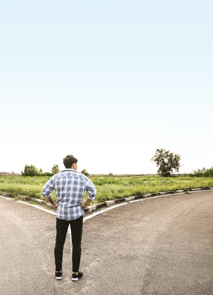 A man standing at a fork in the road, looking at two paths ahead