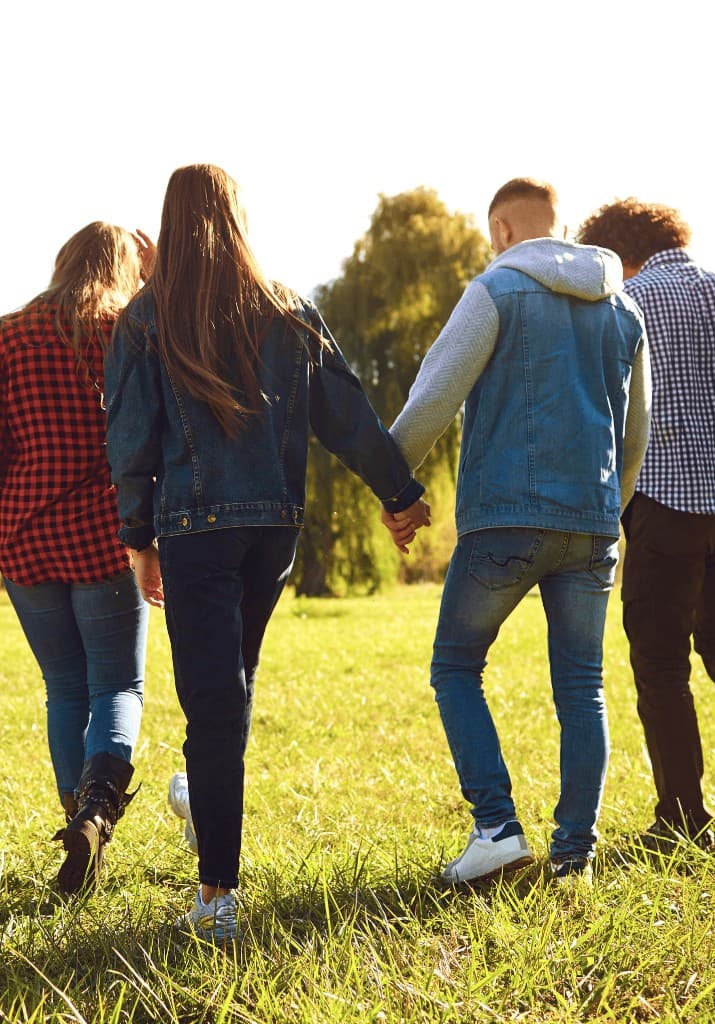 Four young people walking together through a sunlit field
