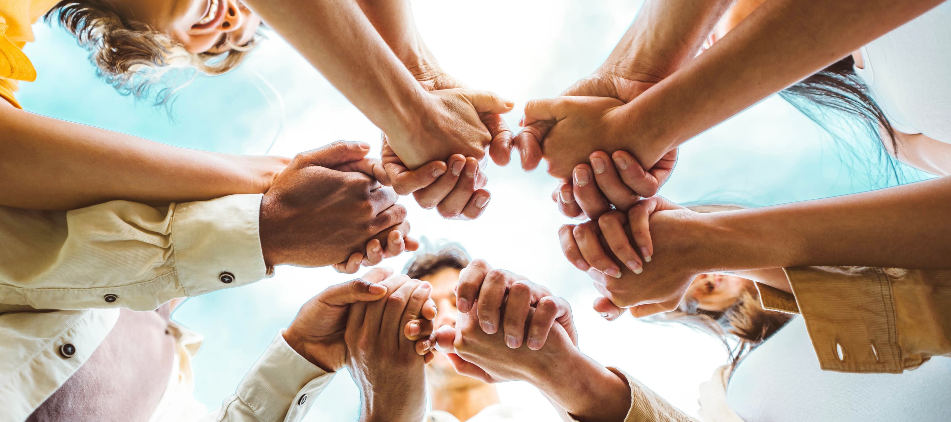 Diverse group joining hands in a circle under a bright sky