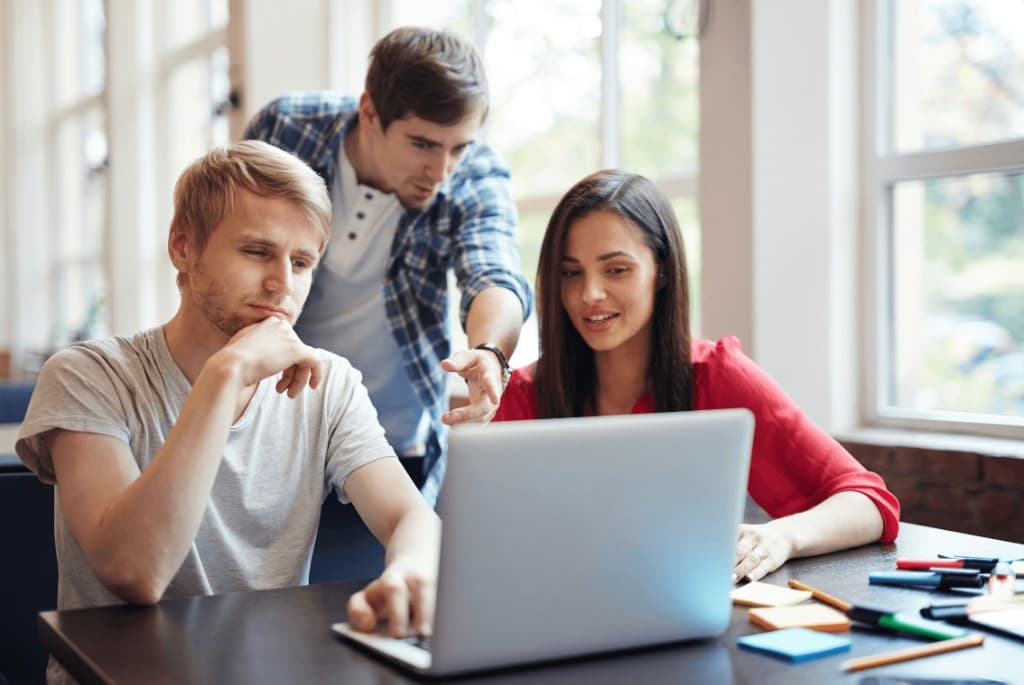 Three young adults collaborating around a laptop with sticky notes on the table